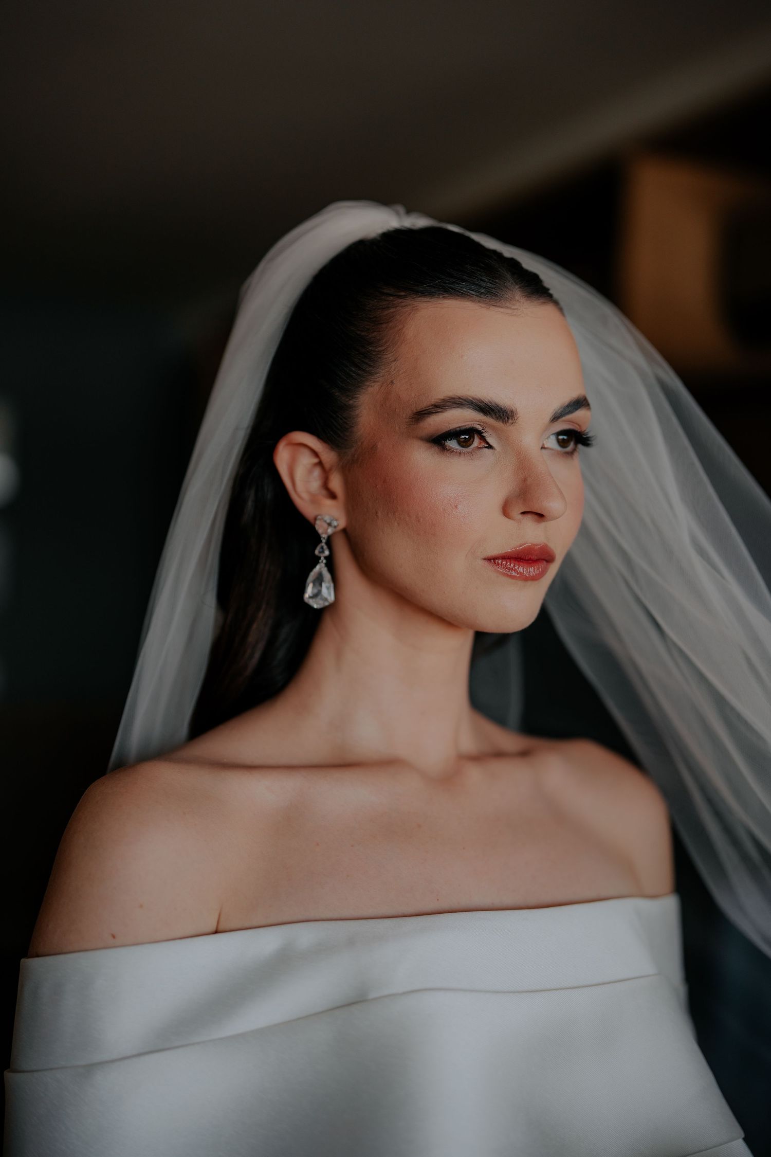 Bride wearing classic off-shoulder gown with delicate veil and crystal earrings.