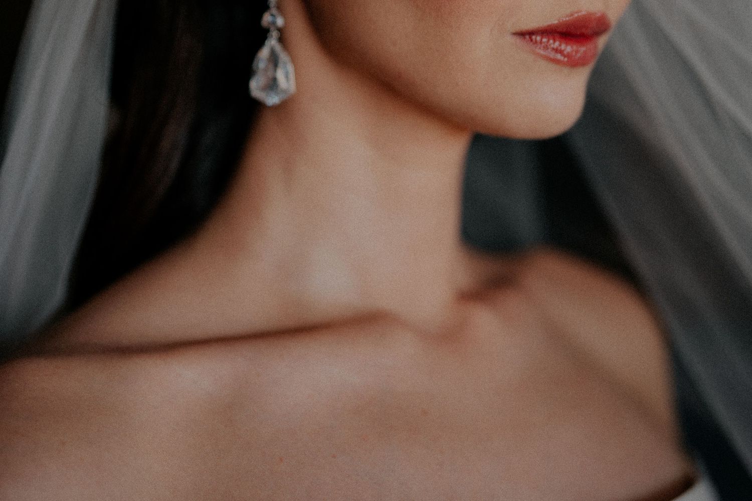 Close-up detail of bridal jewelry and veil against soft lighting.