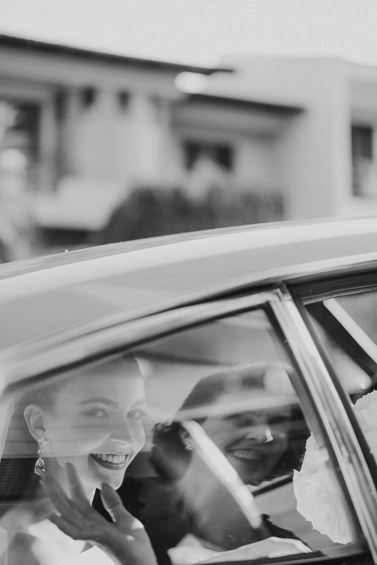 Wedding party laughs joyfully while sitting in a car during celebration.