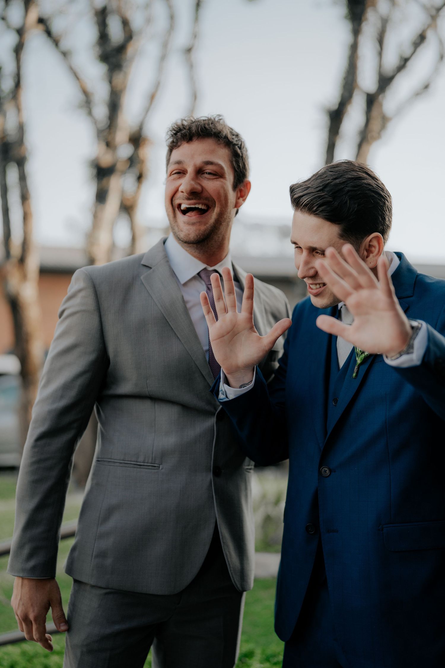 Groomsmen in suits share laughs and smiles outside during wedding festivities.