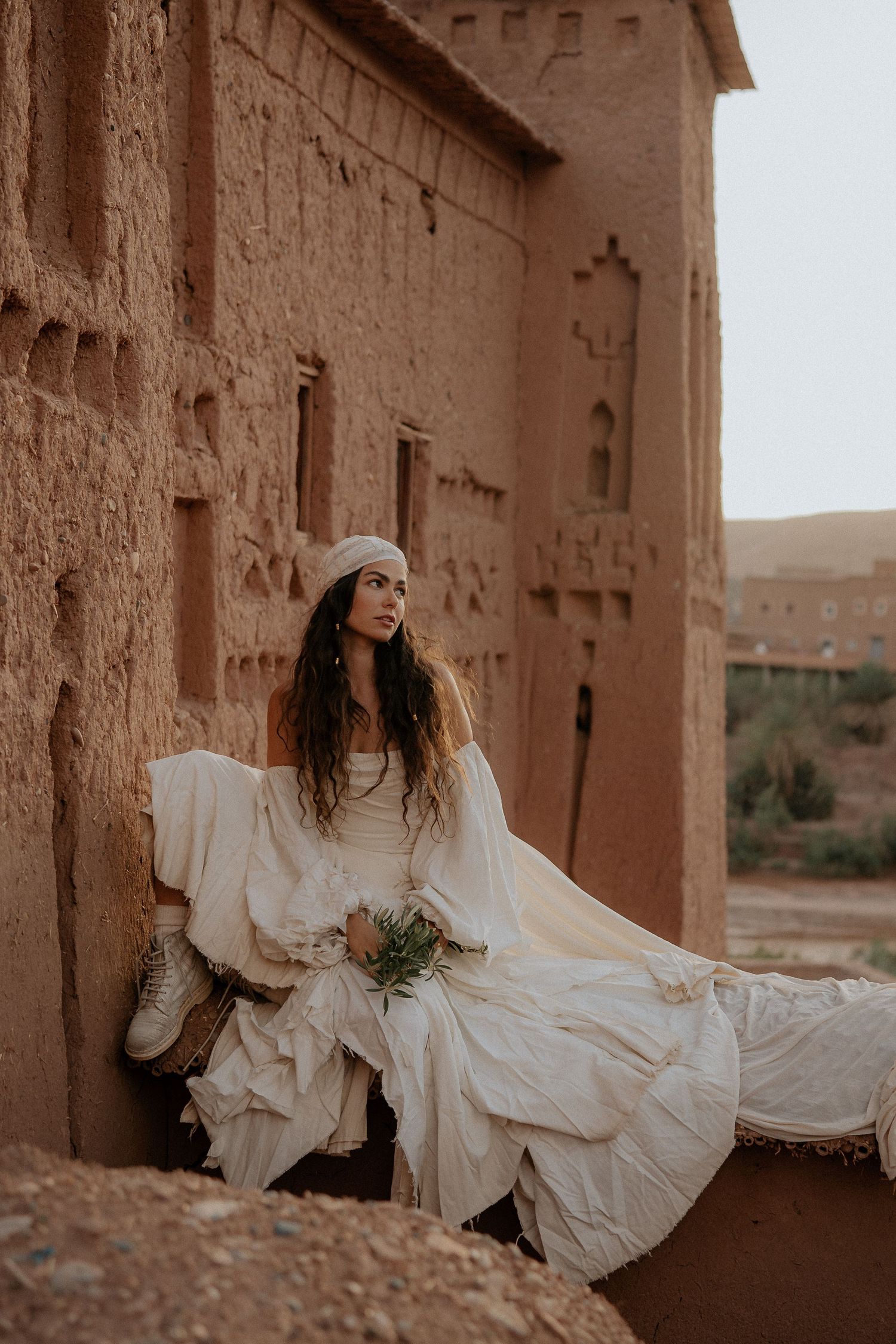 White dress creates graceful silhouette against earth-toned desert fortress walls.
