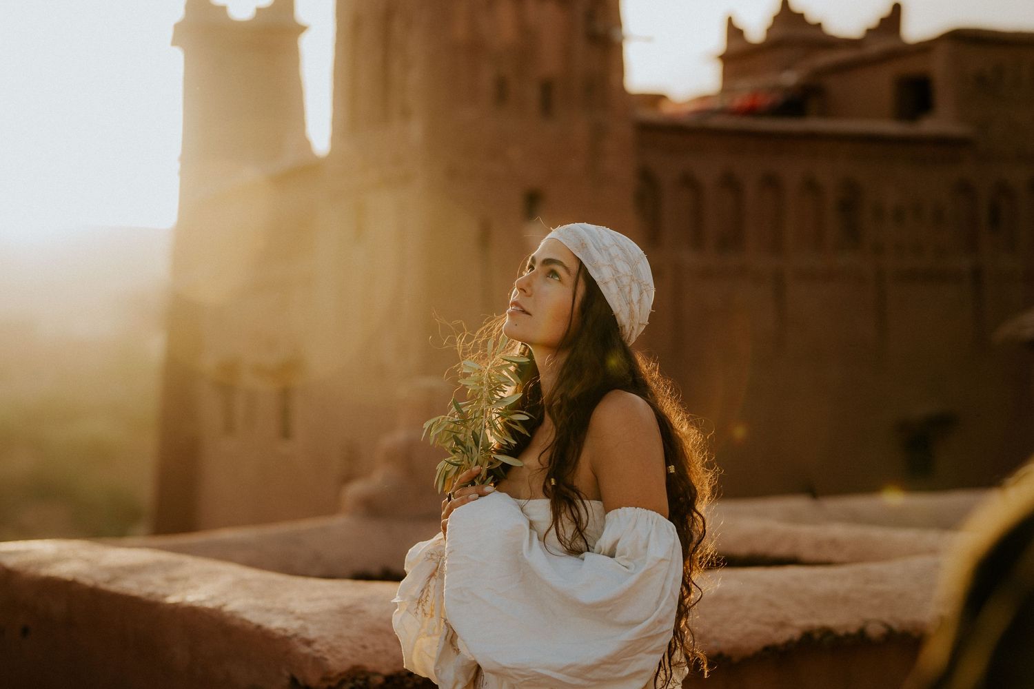 Dreamy sunset photoshoot with flowing white fabric against desert fortress backdrop.