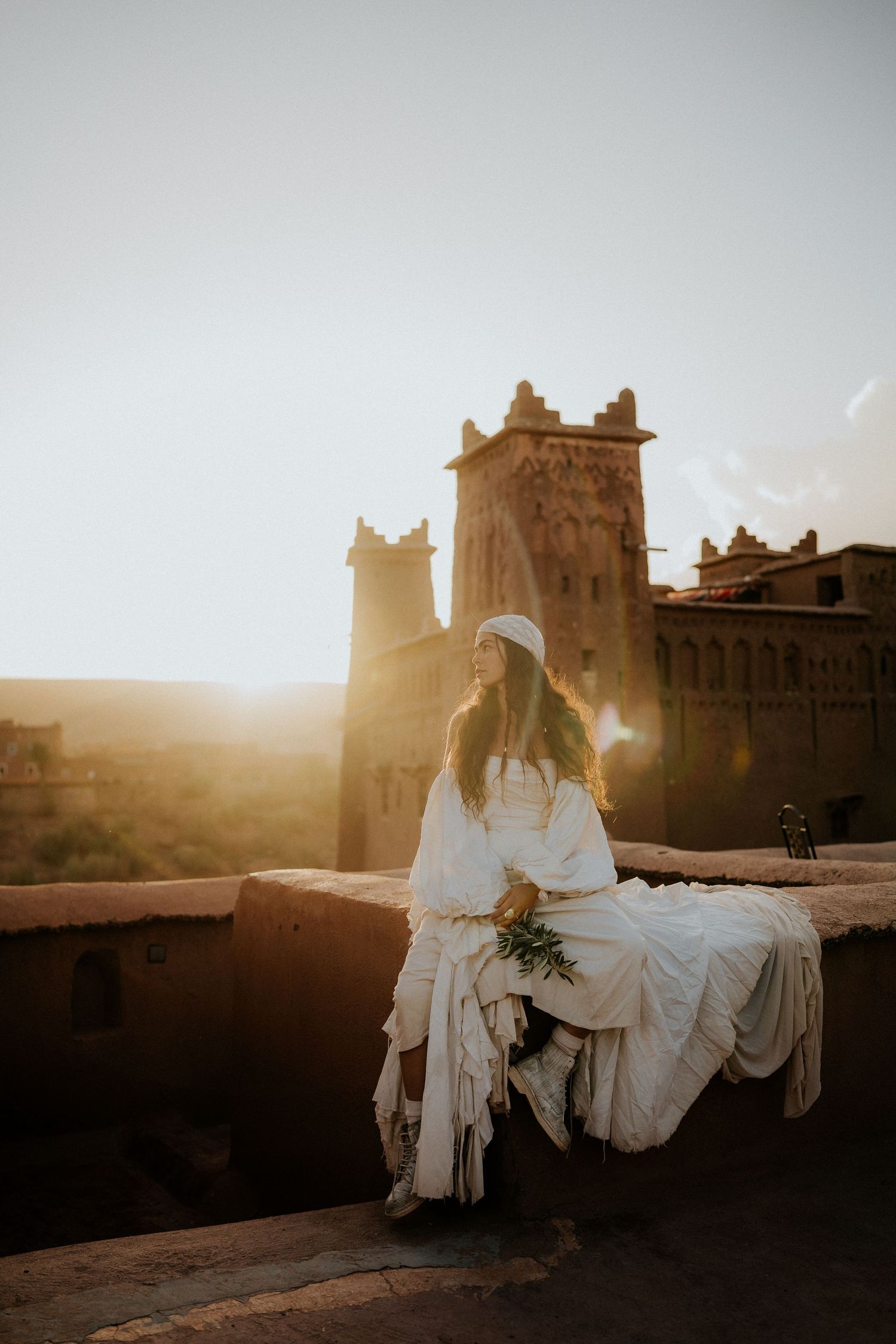 Sunset glow illuminates white-dressed figure against ancient desert fortress.