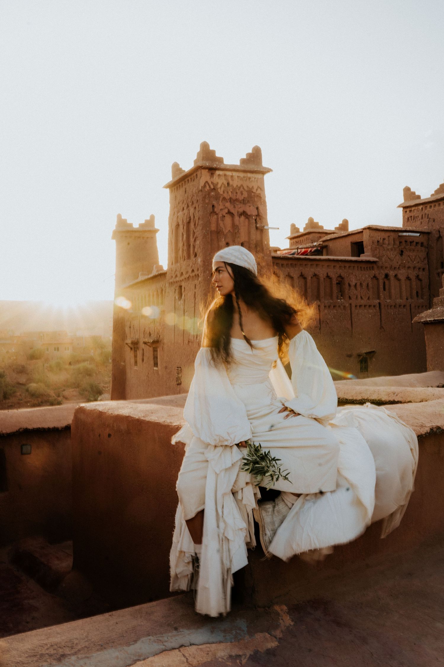 Golden hour light bathes desert kasbah setting with flowing white fabric in motion.