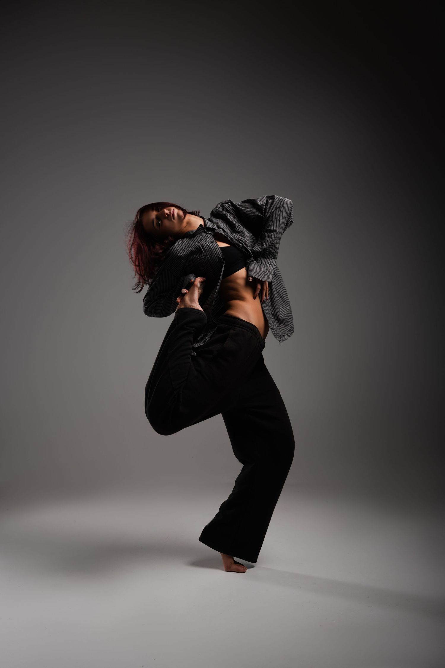 Contemporary dancer performs fluid movement sequence in dramatic lighting with dark clothing against grey backdrop.