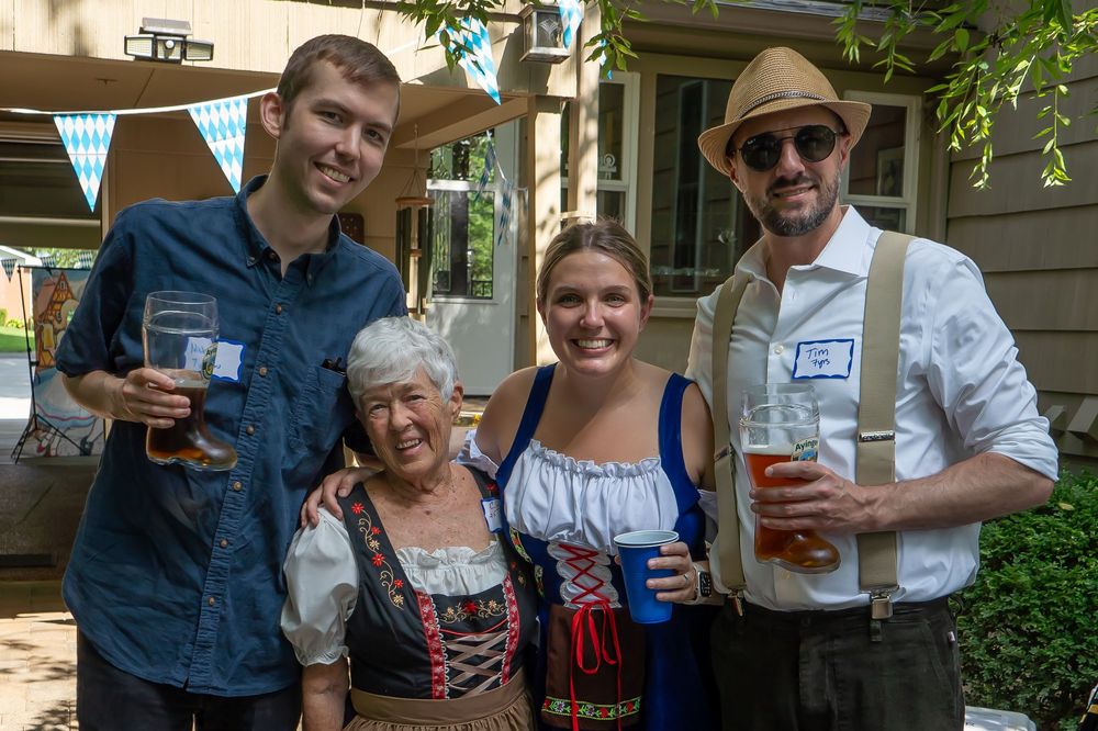 People in traditional German clothing celebrate at an Oktoberfest party with drinks and decorative bunting in the background.