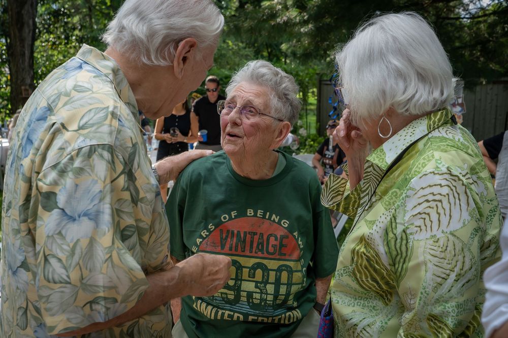 Casual conversation at an outdoor gathering among people wearing light summer clothing and floral prints.