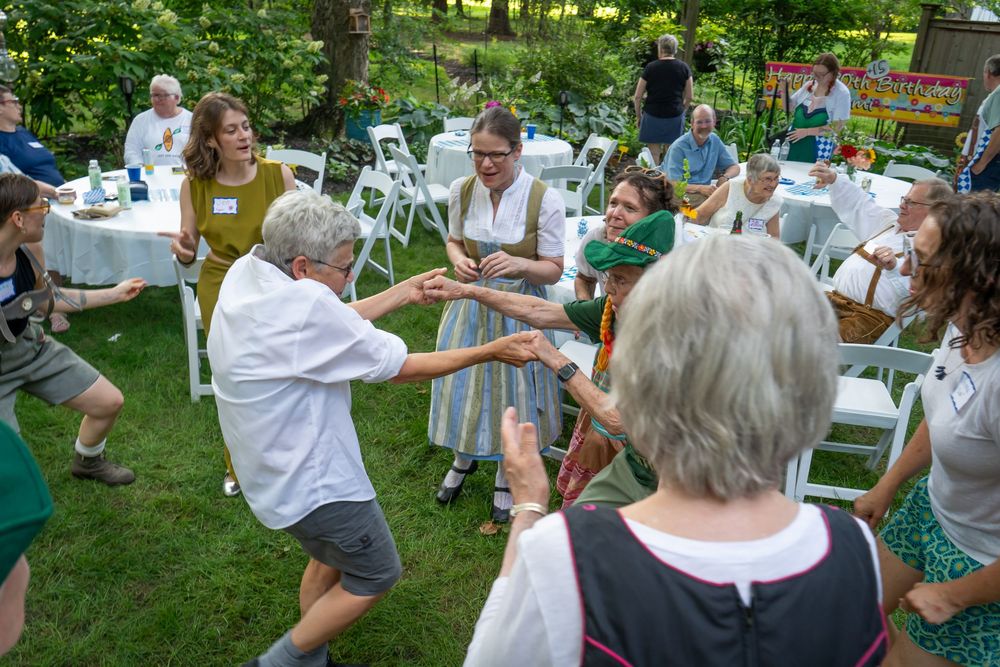 People dancing and socializing together at an outdoor garden party with white tablecloths and greenery in background.