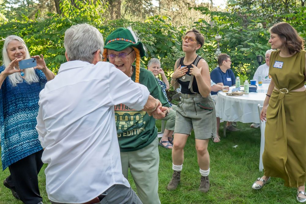 People celebrating and dancing outdoors during a festive summer gathering in a backyard garden setting.