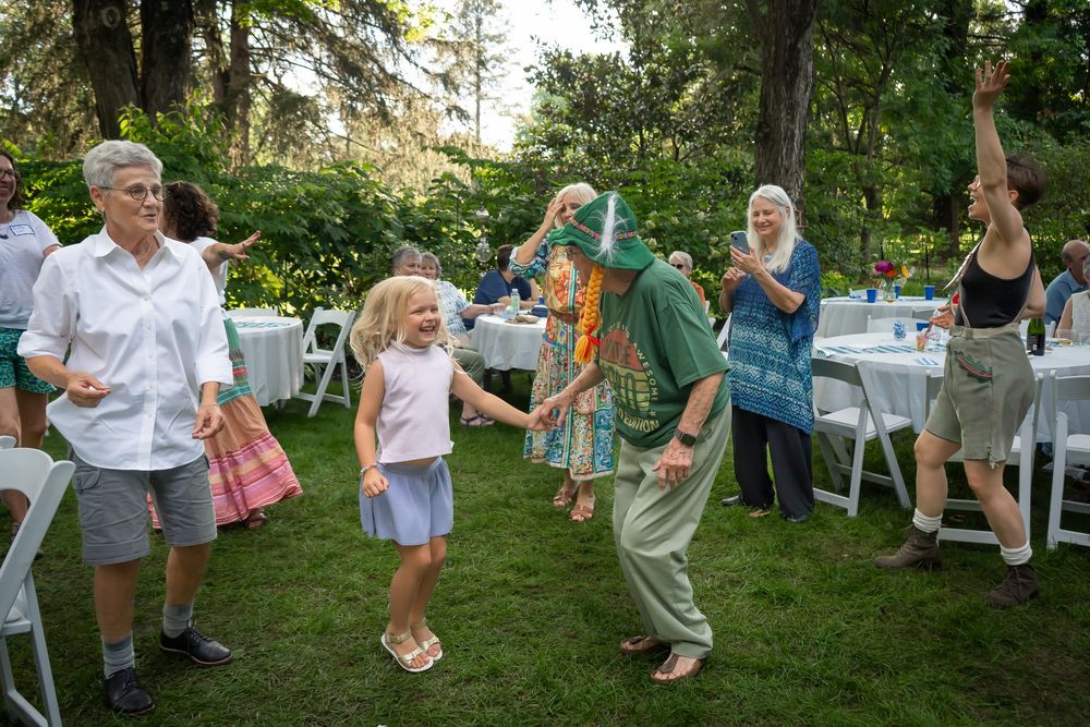People gathered outdoors in a garden setting during a summer dance party with decorative string lights.