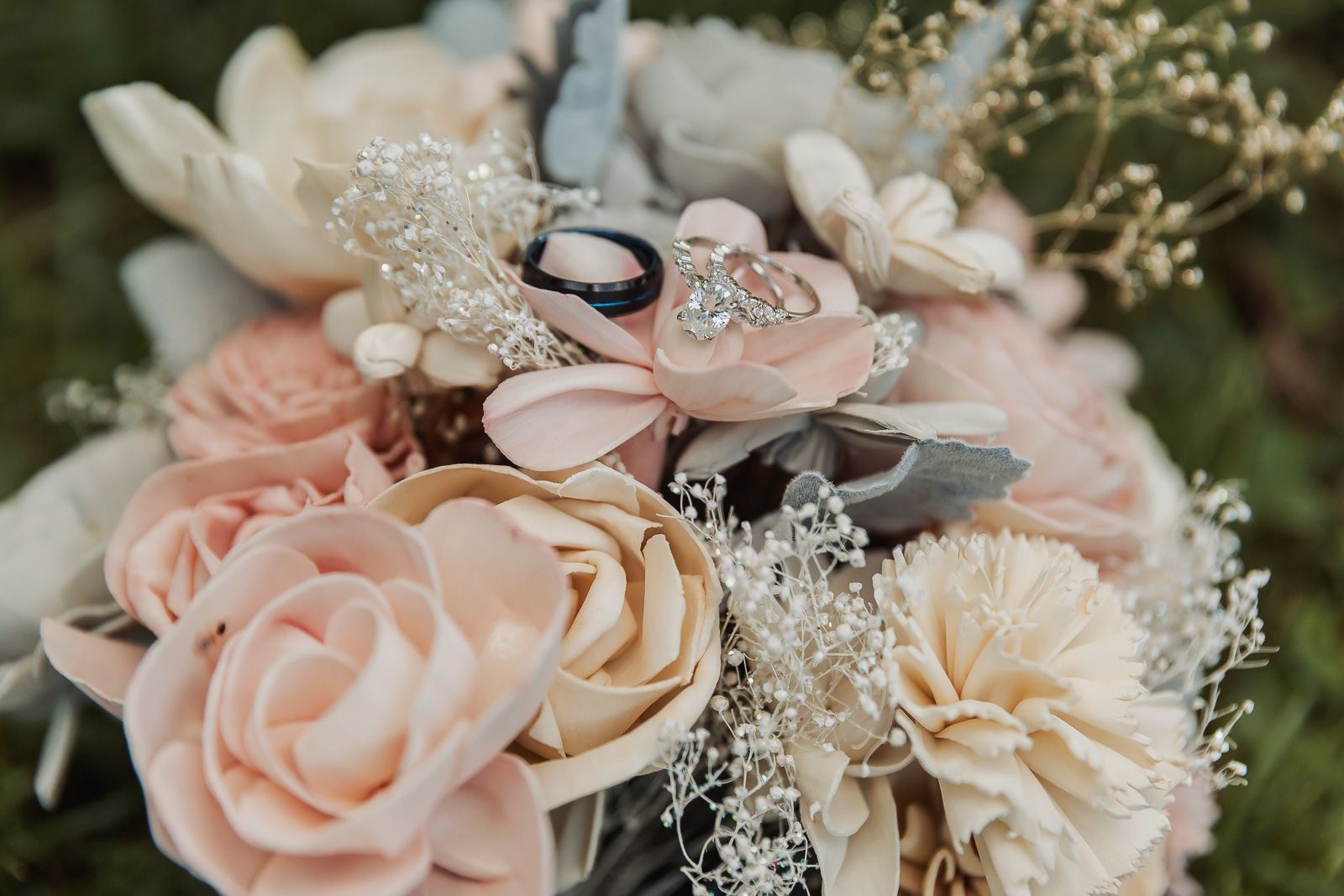 Wedding rings rest on blush pink and cream roses with delicate baby's breath in a romantic floral arrangement.