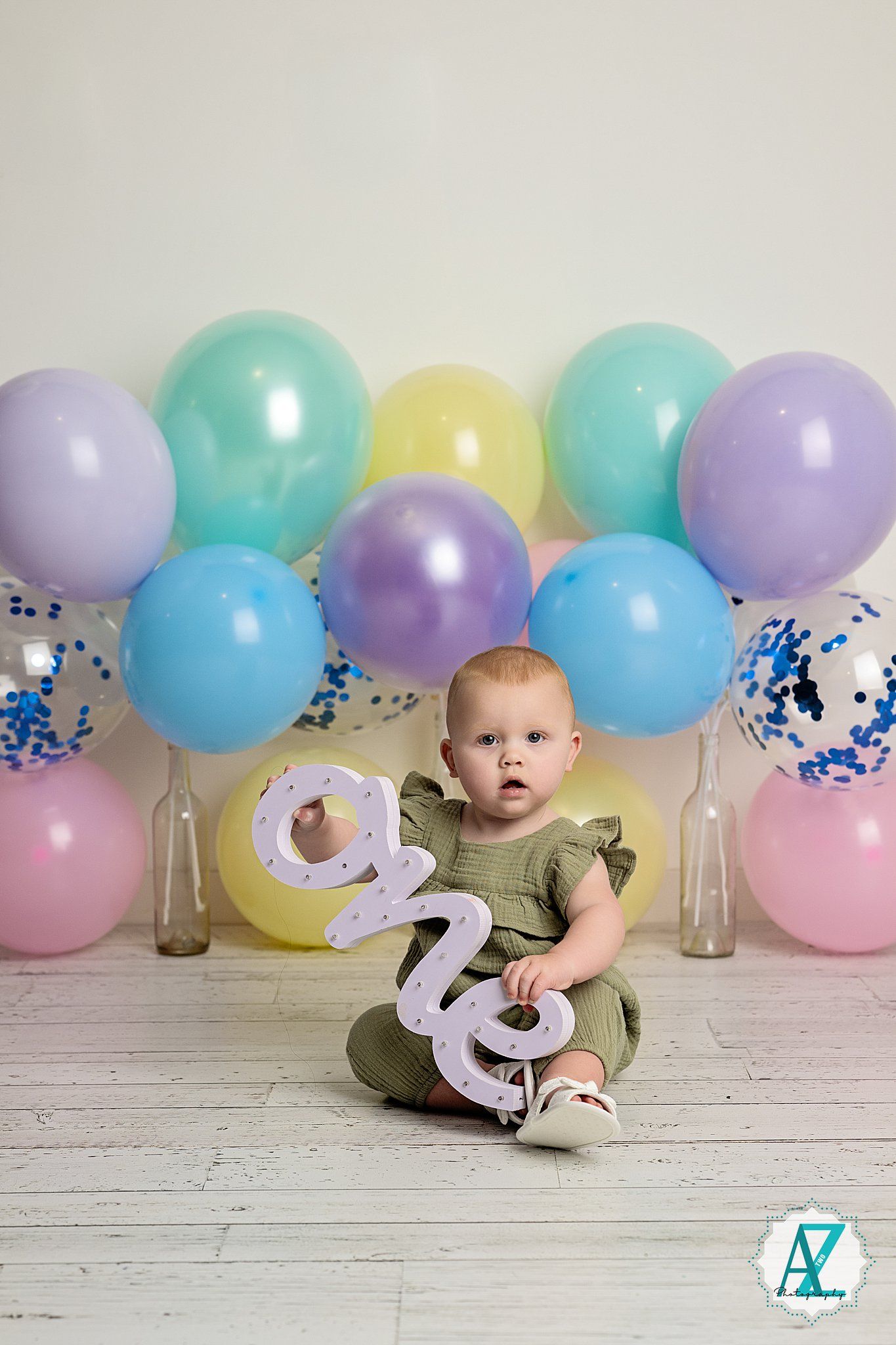 Birthday setup with pastel balloons and silver number decorations against a white wooden backdrop.