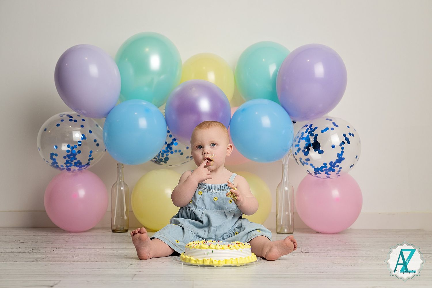 Festive cake smash photo setup with pastel balloons and confetti arranged on white floor.