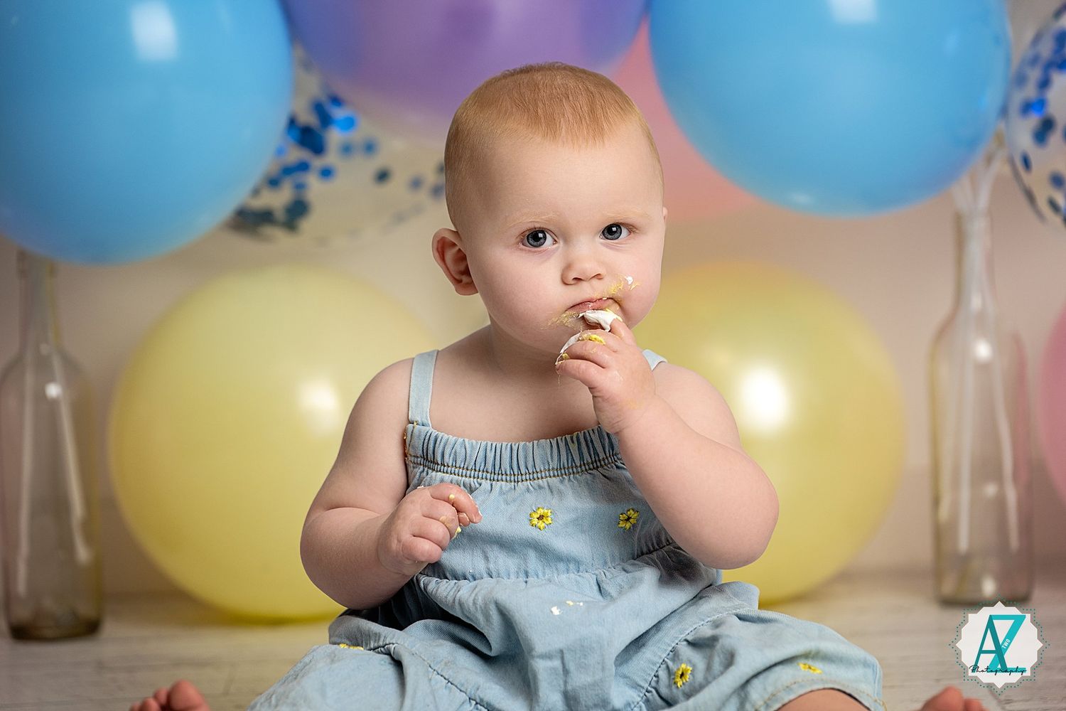 First birthday celebration scene with blue and purple balloons and a small yellow cake.
