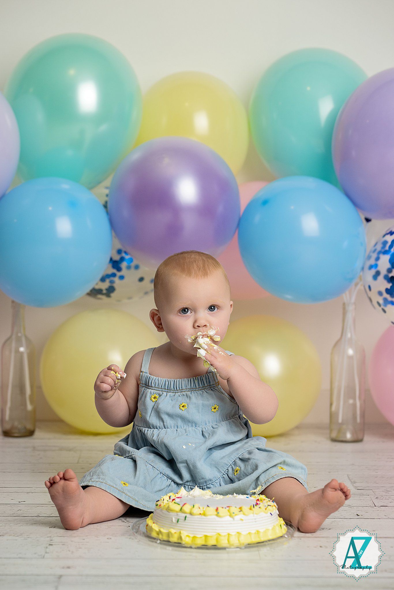 First birthday cake smash photo session with pastel balloons and yellow frosted cake.