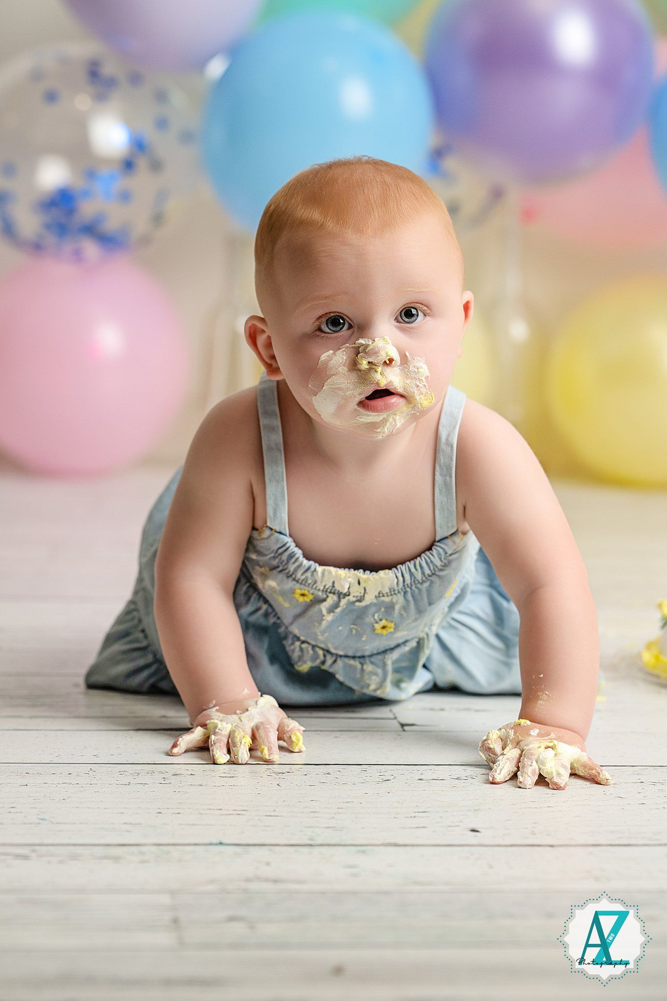 Crawling baby wearing light blue romper surrounded by pastel party balloons.