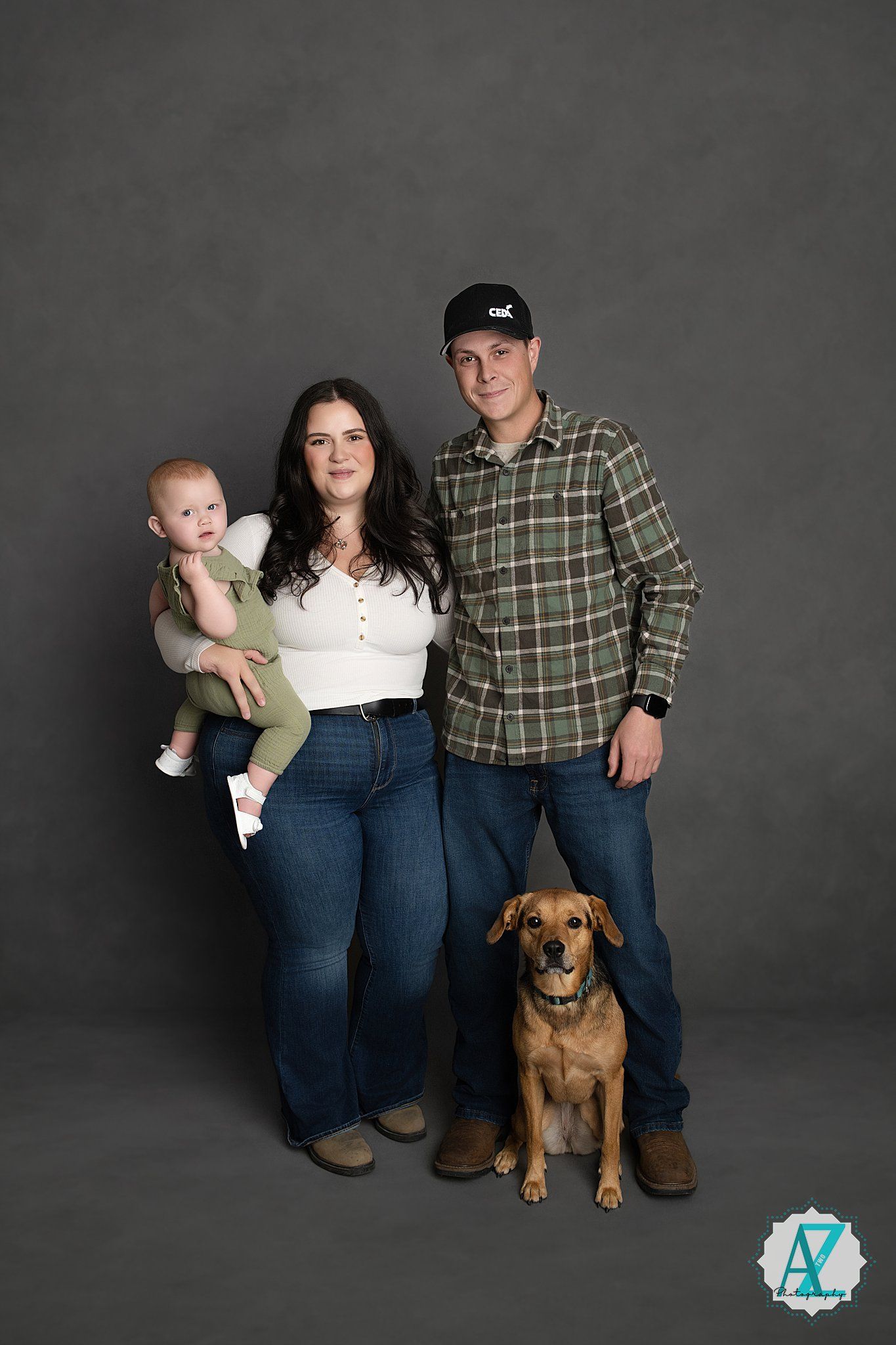 Family portrait with their brown dog against a dark gray studio backdrop.