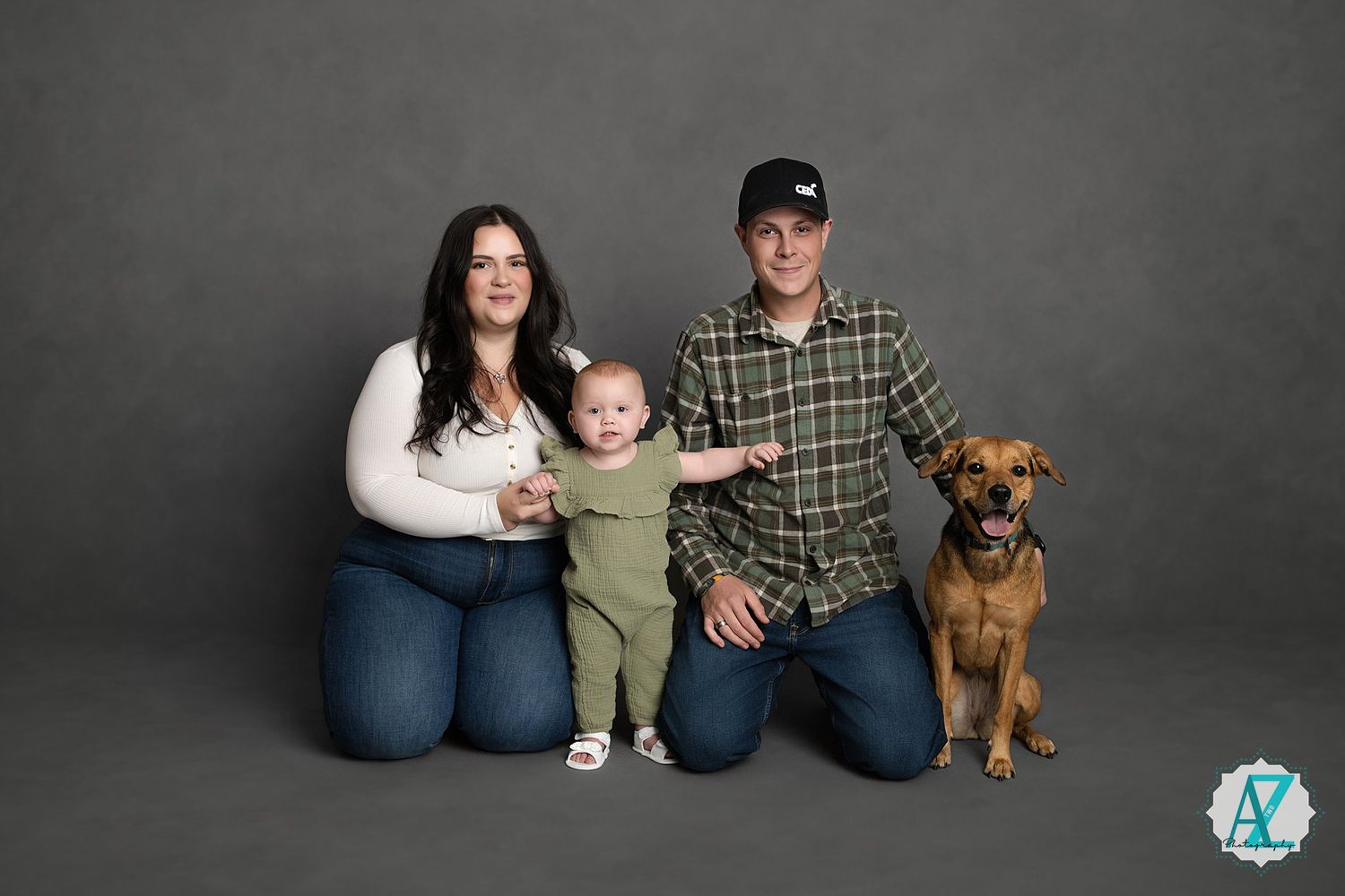 Family portrait with dog against grey backdrop in studio setting.