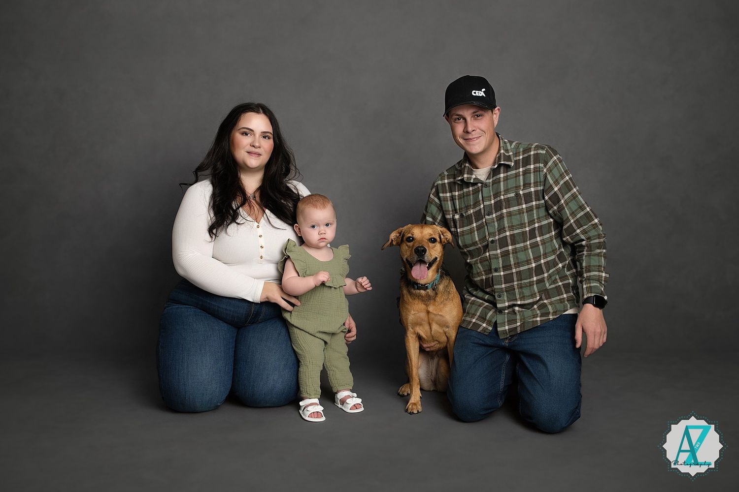 Modern family portrait with dog against dark grey background showing casual lifestyle setting.