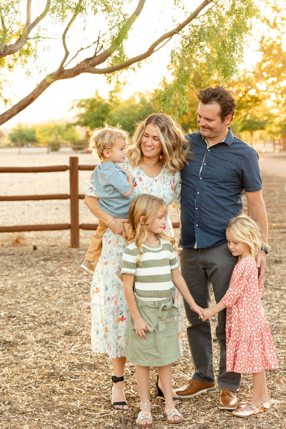 southern utah family photos of 5 with 3 little kids 2 girls one boy smiling at each other under a tree with a farm in the background