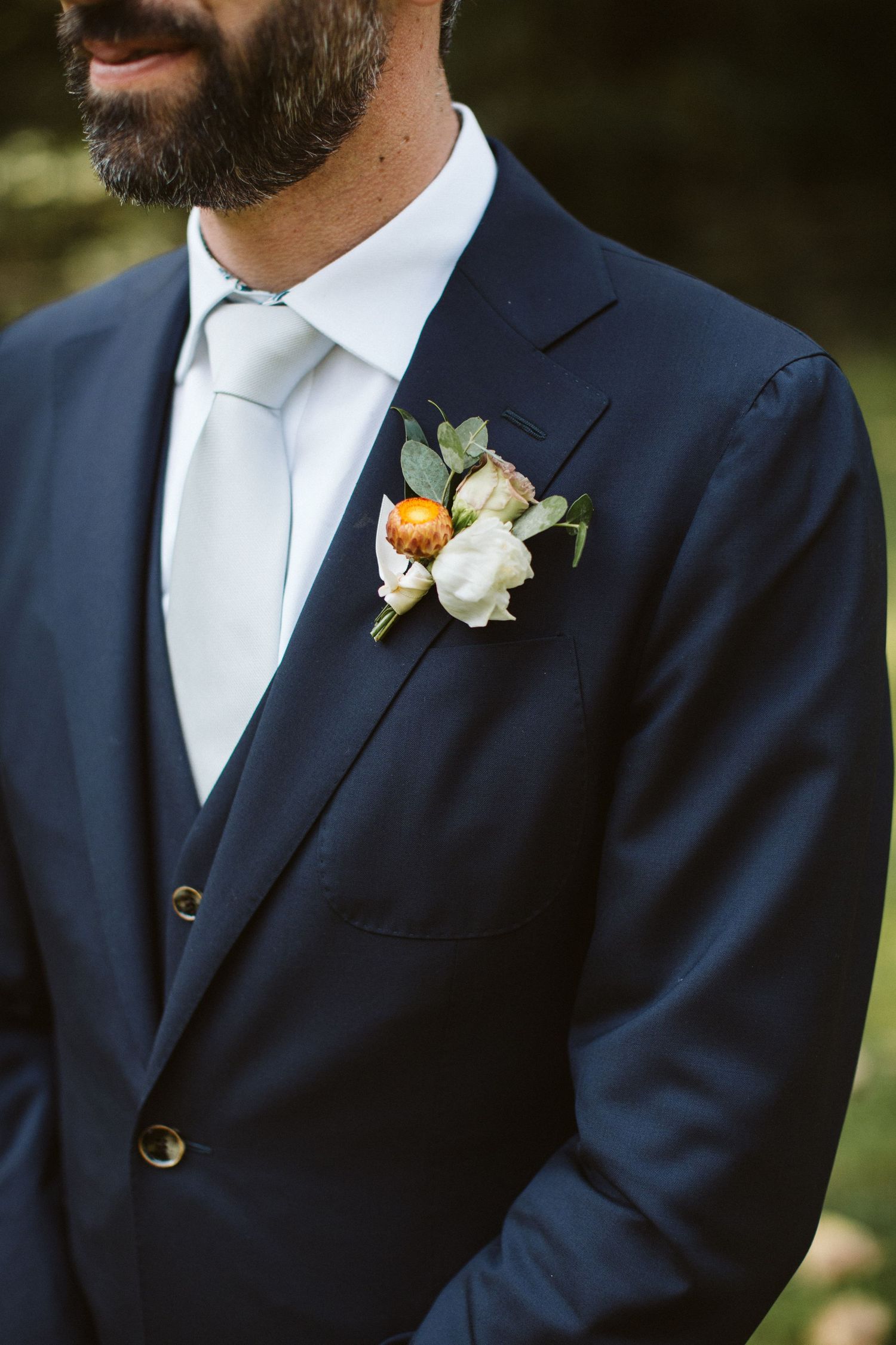 Detail of navy suit with floral boutonniere and white tie.