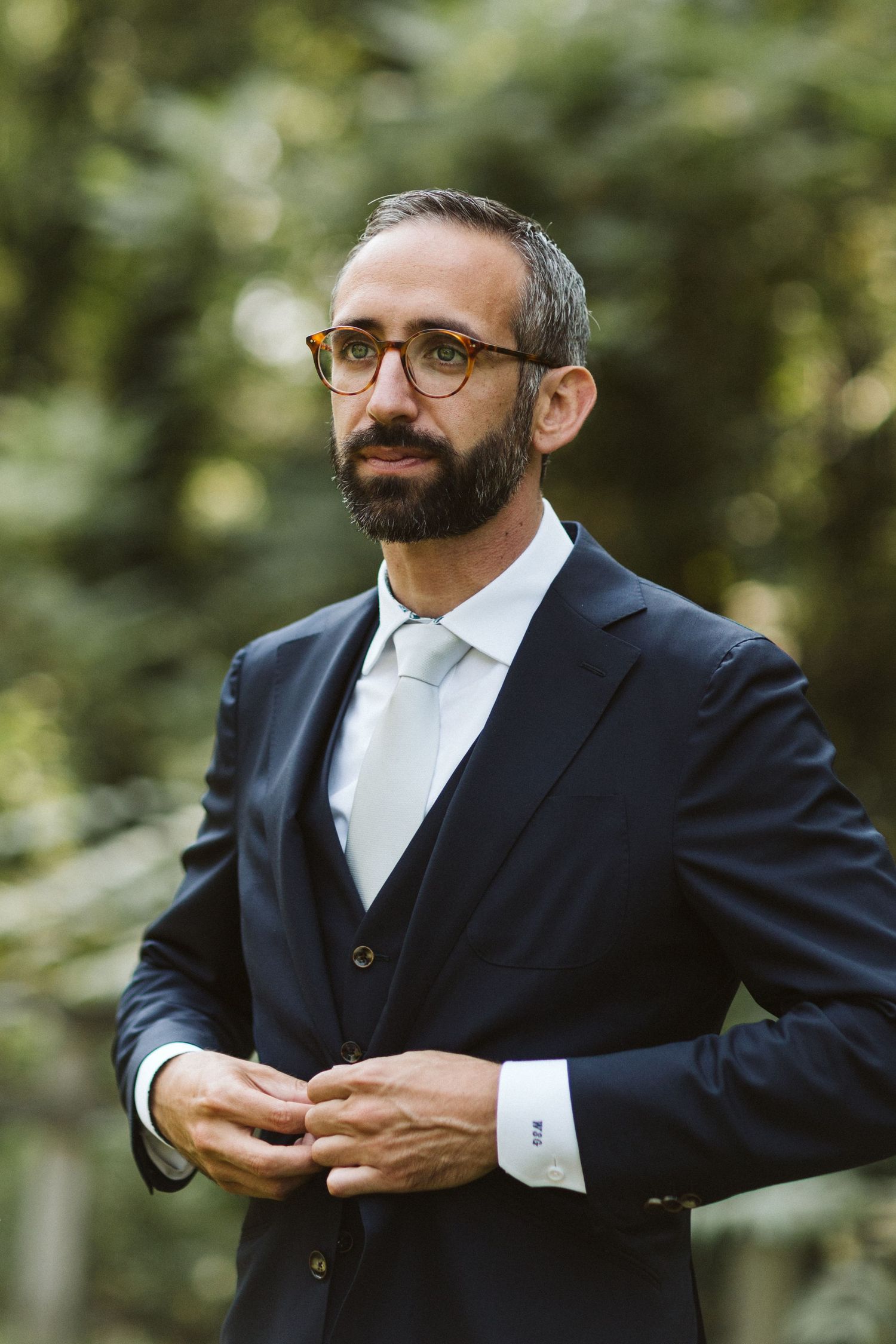 Groom in navy suit adjusting cuffs and boutonniere.