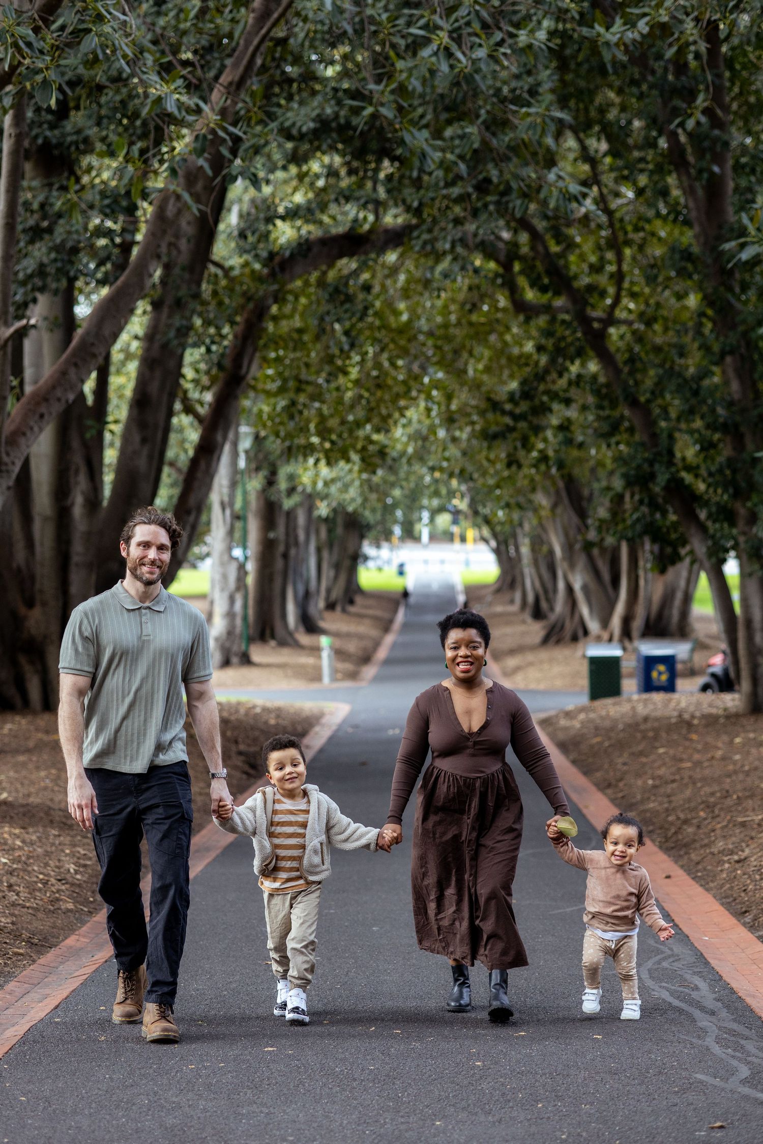 Young family walking hand-in-hand through Treasury Gardens, Melbourne, capturing a joyful moment in a scenic outdoor setting.