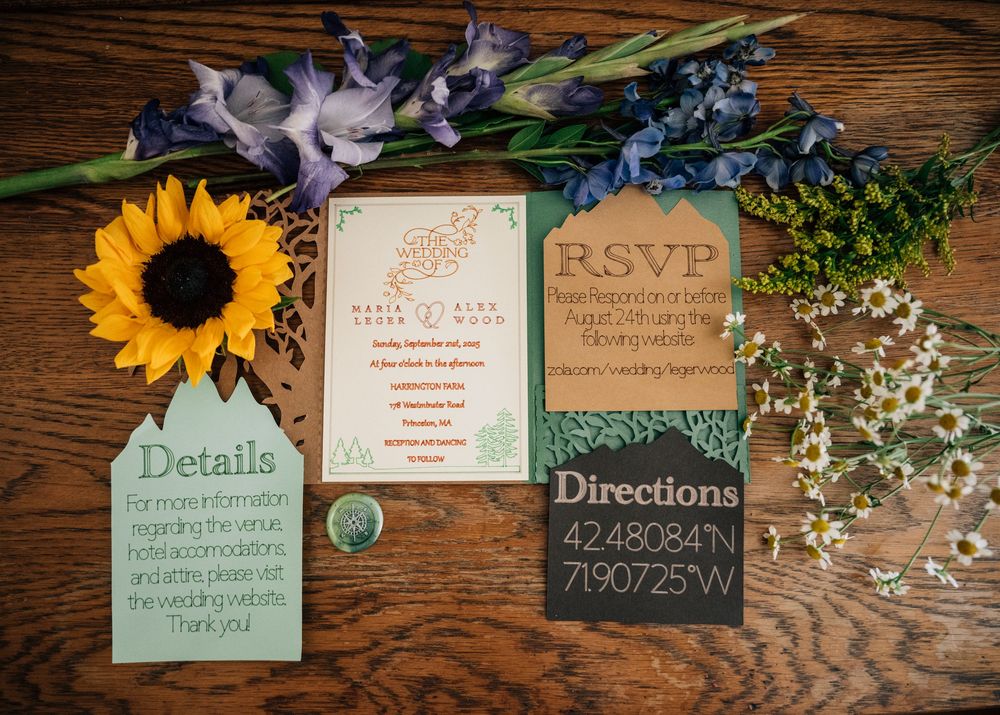Wedding invitation suite with sunflowers and purple flowers arranged on wooden surface.