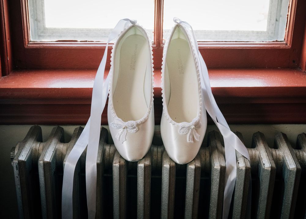 White bridal shoes displayed on a vintage radiator near a window.