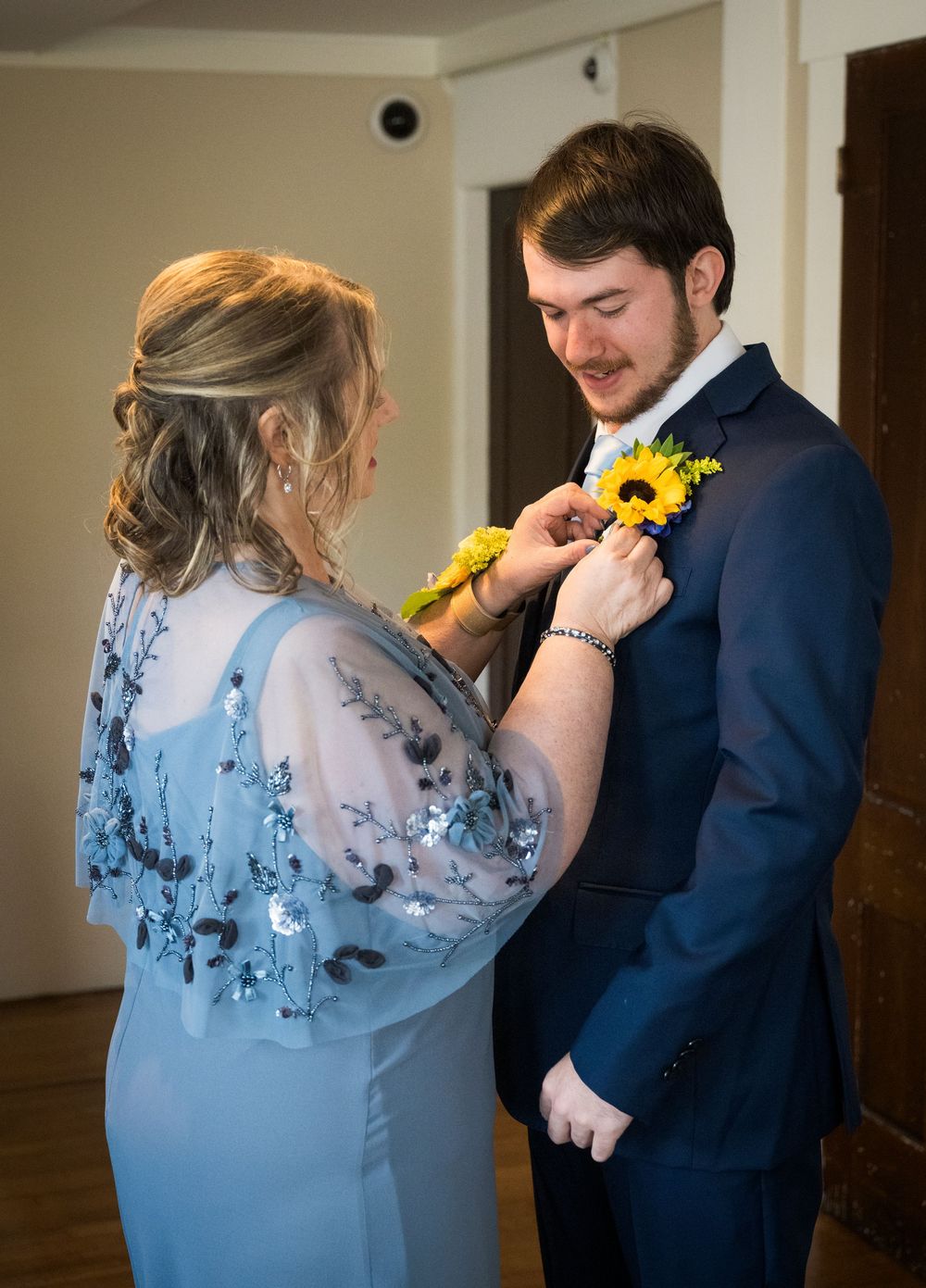A sunflower boutonniere being pinned on a navy suit during wedding preparations.
