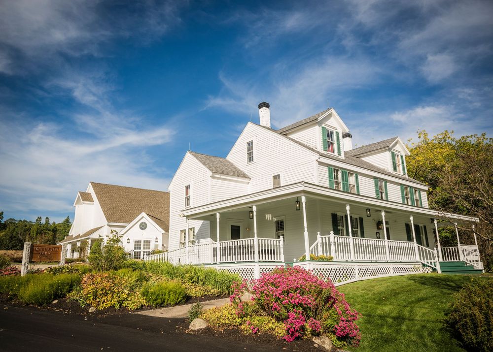 Panoramic view of a white colonial-style wedding venue with wraparound porch under blue skies.
