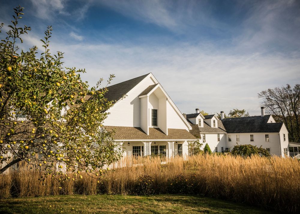 A white farmhouse style venue with dormers set against a dramatic blue sky and tall grass.