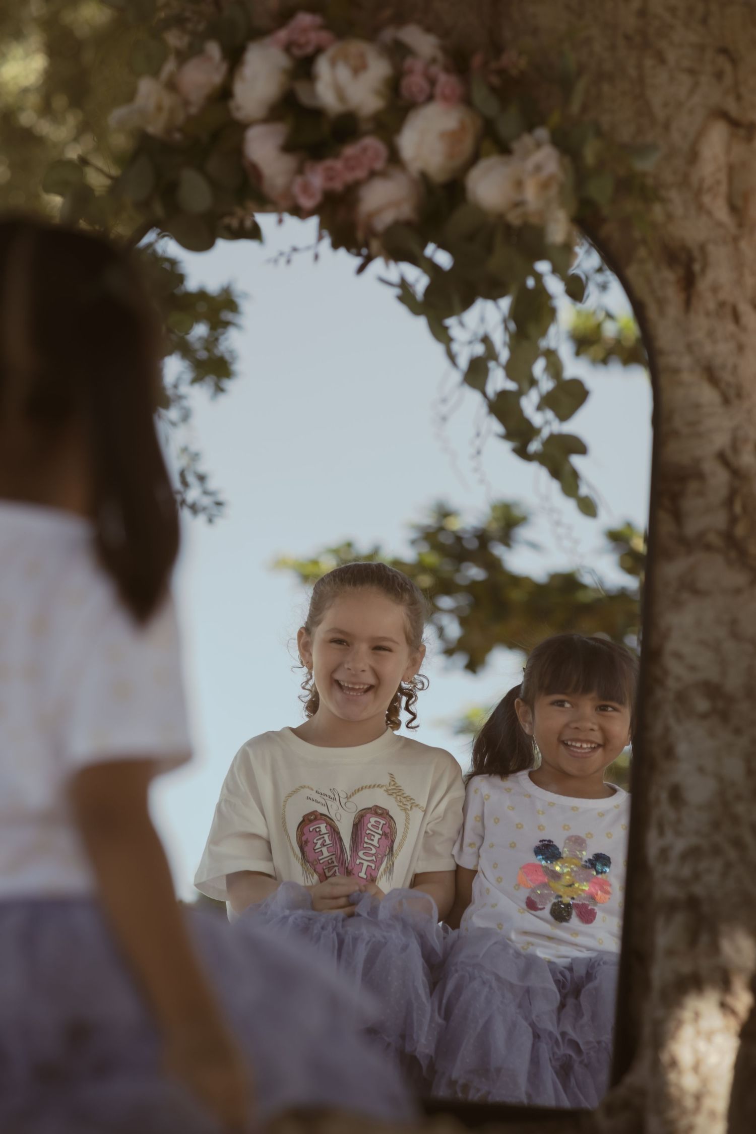 Children playing and laughing together under large tree branches.