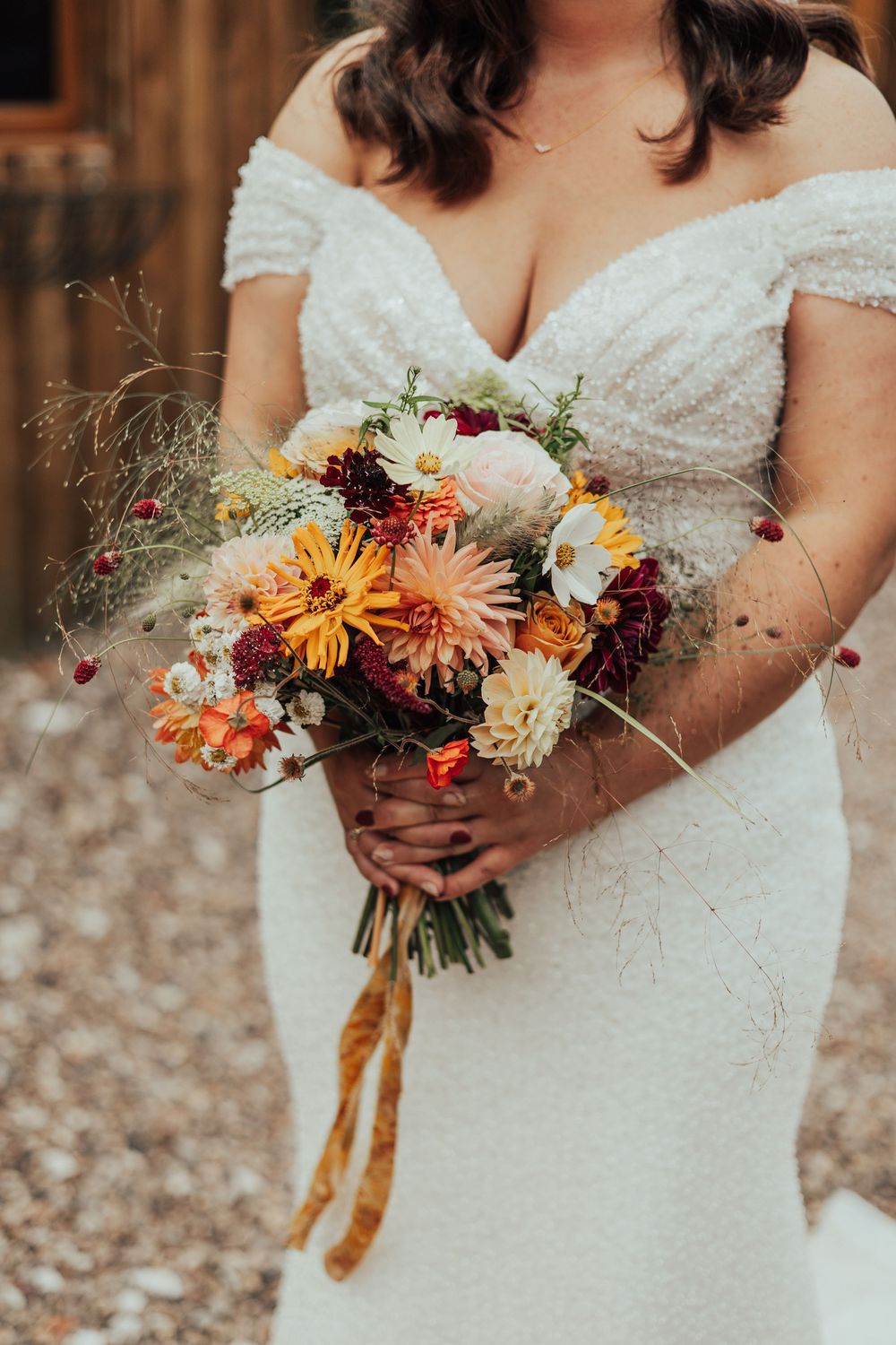 A stunning bridal bouquet with orange and white flowers held against a beaded white wedding dress.