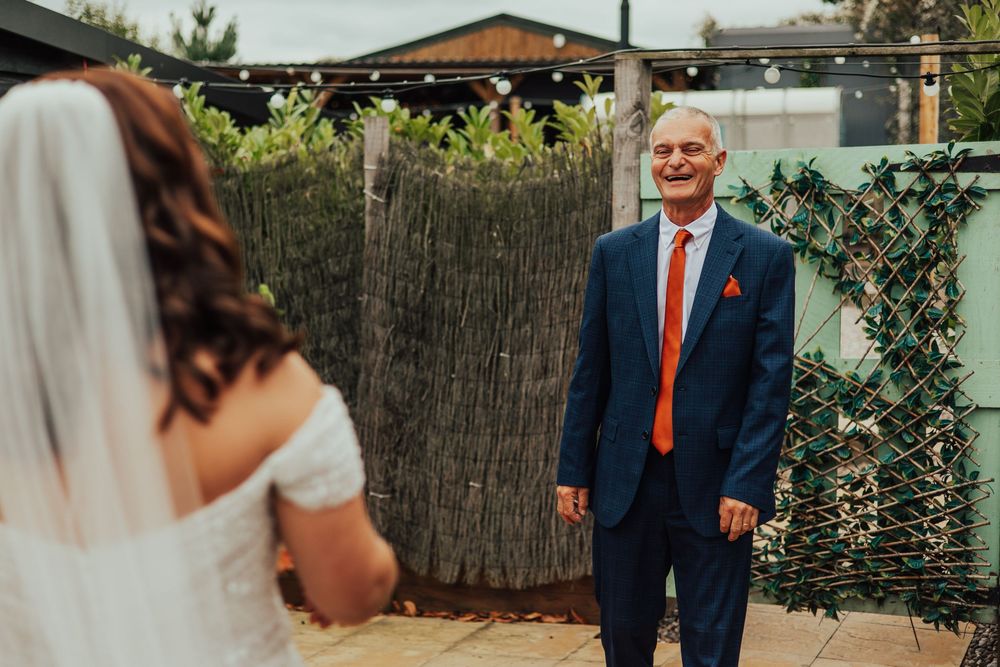Elegant wedding couple embraces in a lush garden setting with guests and family members gathered nearby.