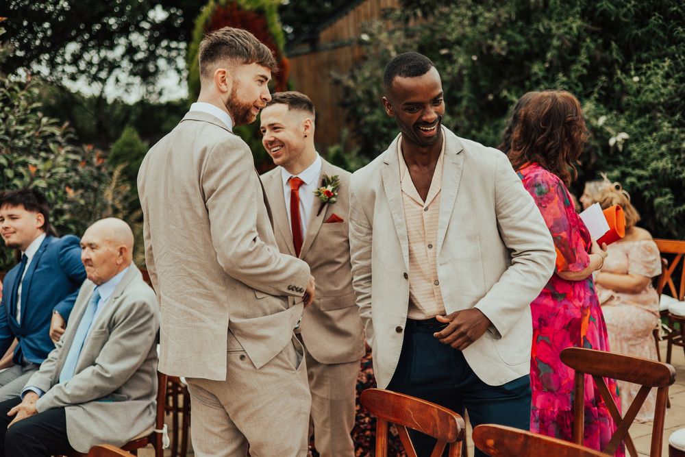 A group of groomsmen in beige suits share a joyful moment at an outdoor wedding celebration.