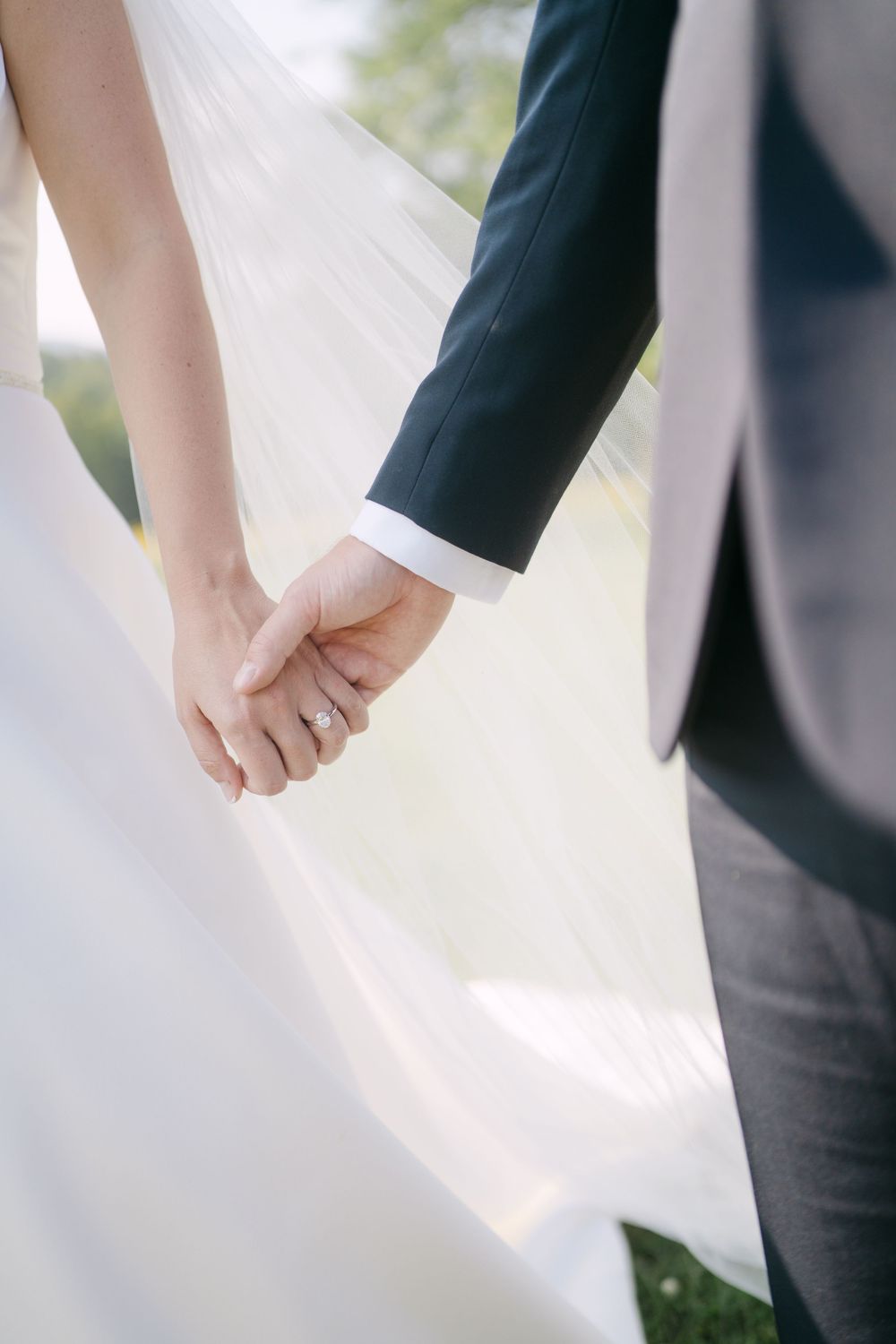 Close-up details of bride and groom holding hands in wedding attire.