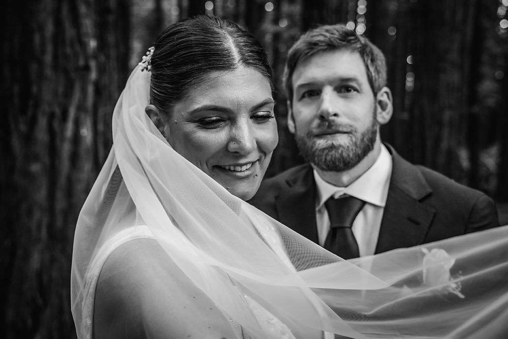 A bride in white laughs and smiles while caught in a candid moment during a forest wedding photoshoot.