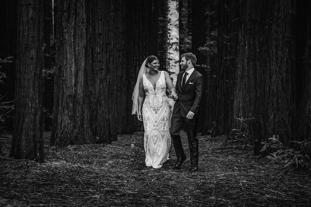 A romantic black and white photo series captures a couple among towering redwood trees in the forest.