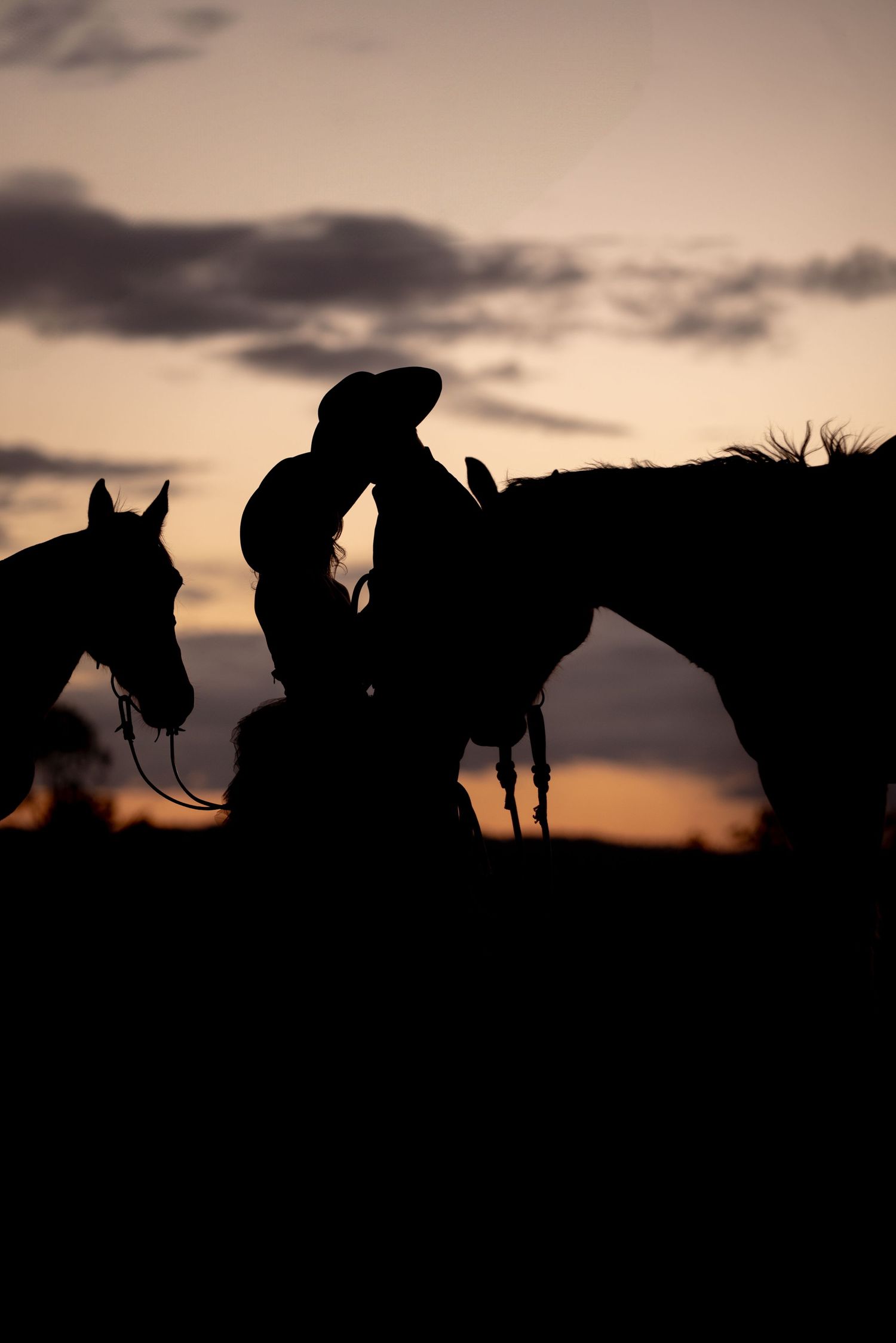Silhouettes of horses and riders against a dramatic sunset sky create a striking western scene on the horizon.