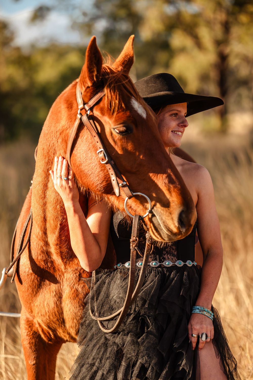 A chestnut horse stands close to its rider during a sun-drenched golden hour photo session in a field.