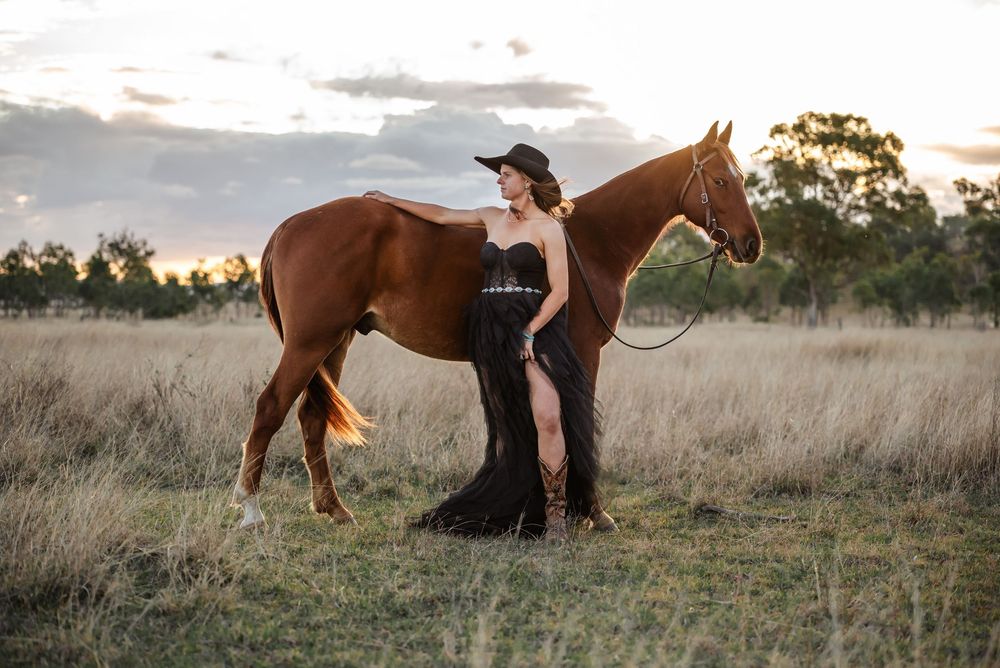 A chestnut horse and rider silhouetted against a dramatic sunset sky in a grassy field.