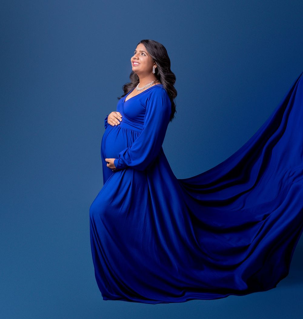 Maternity photo featuring an elegant flowing royal blue dress against a deep blue background.