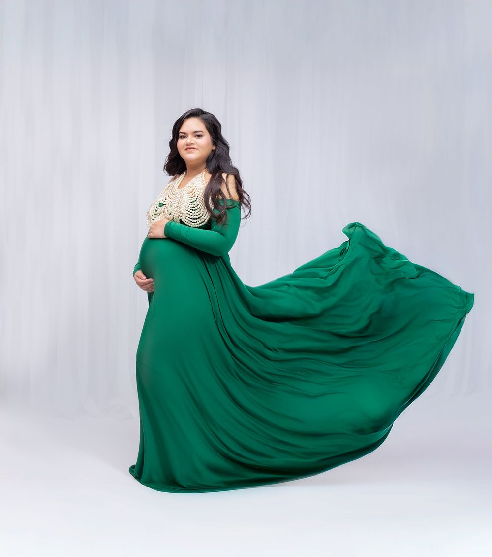 Flowing emerald green gown with dramatic movement captured in a studio setting against a white backdrop.