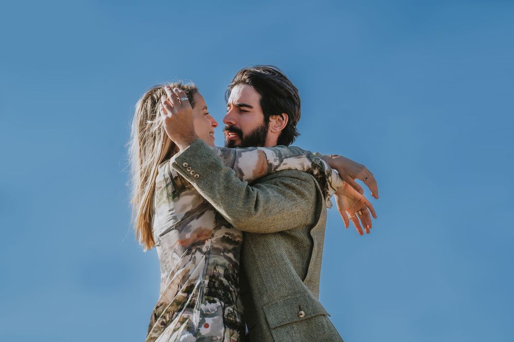 A romantic couple embracing outdoors against a bright blue sky on a sunny day.