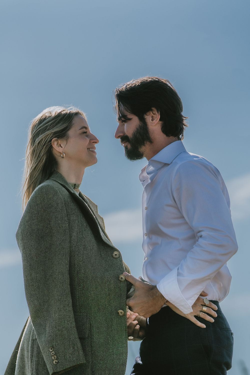 A romantic couple in business casual attire gaze at each other outdoors on a sunny day.