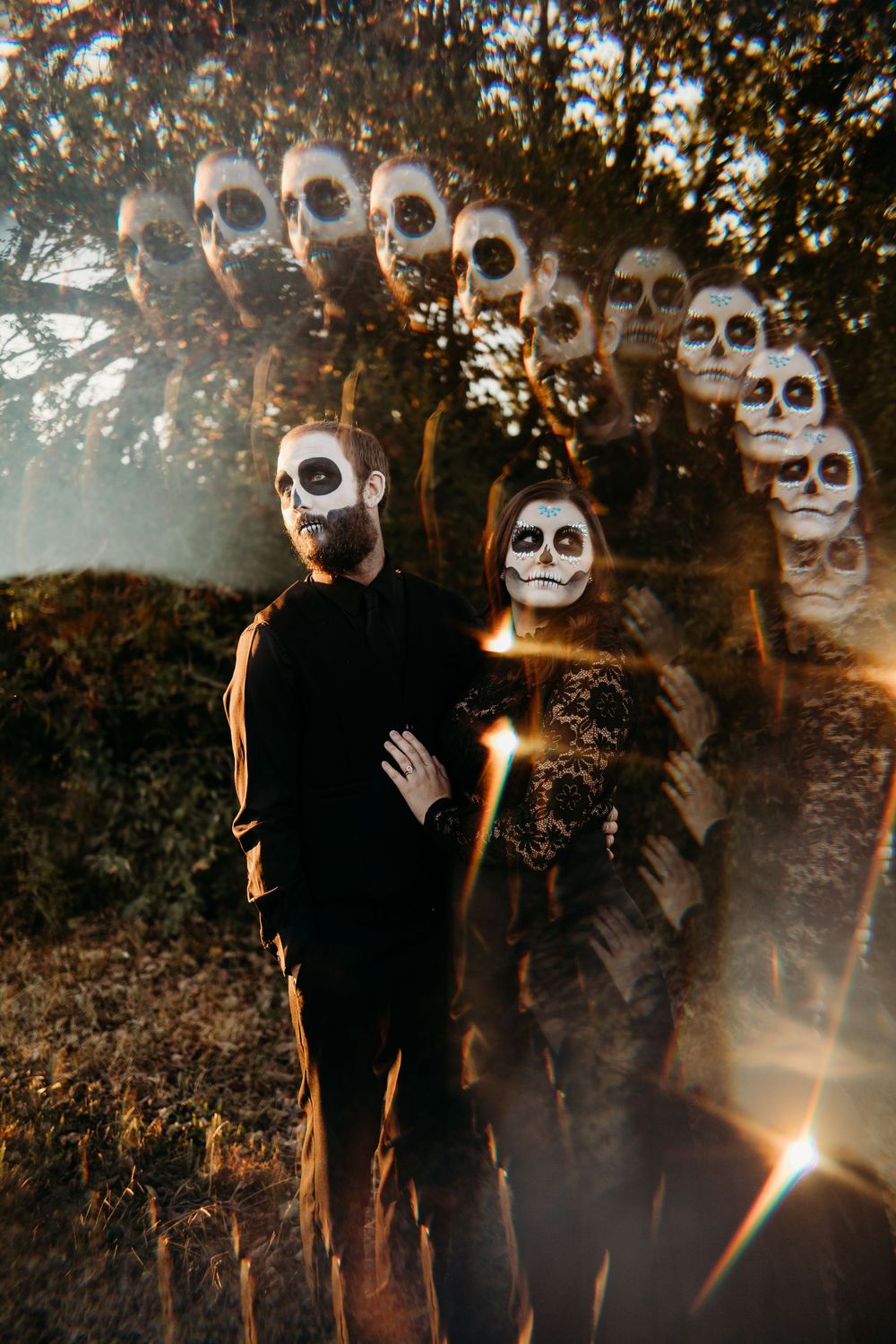 Couple in black outfits with skull face paint pose in forest with eerie double exposure skull effect.