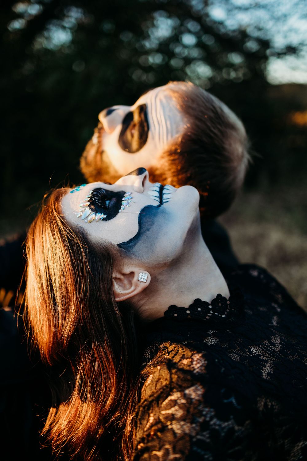 Close-up of couple wearing detailed Day of the Dead sugar skull makeup looking upward in golden light.