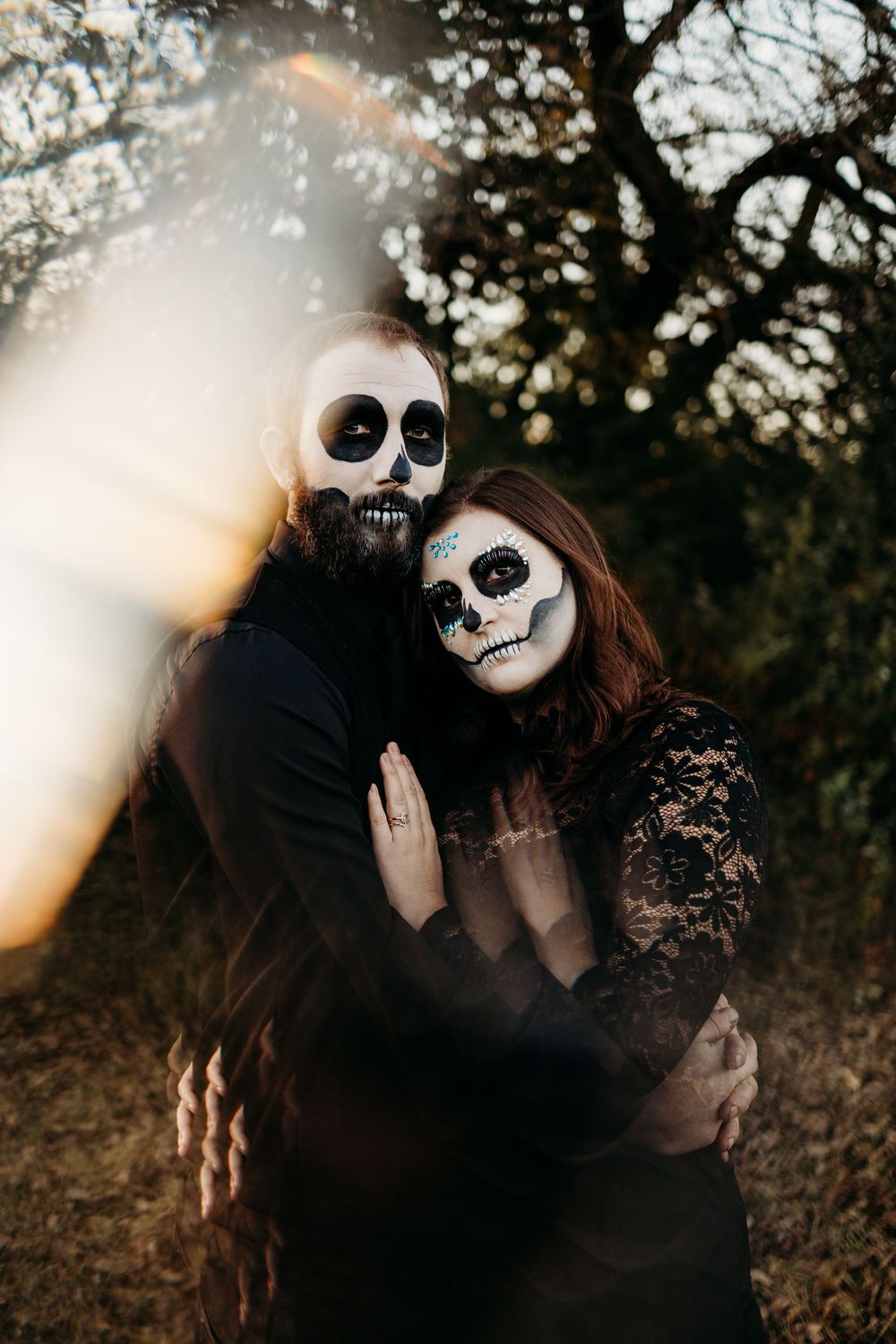 Couple in matching black outfits with skeleton face paint embrace during golden hour in outdoor setting.
