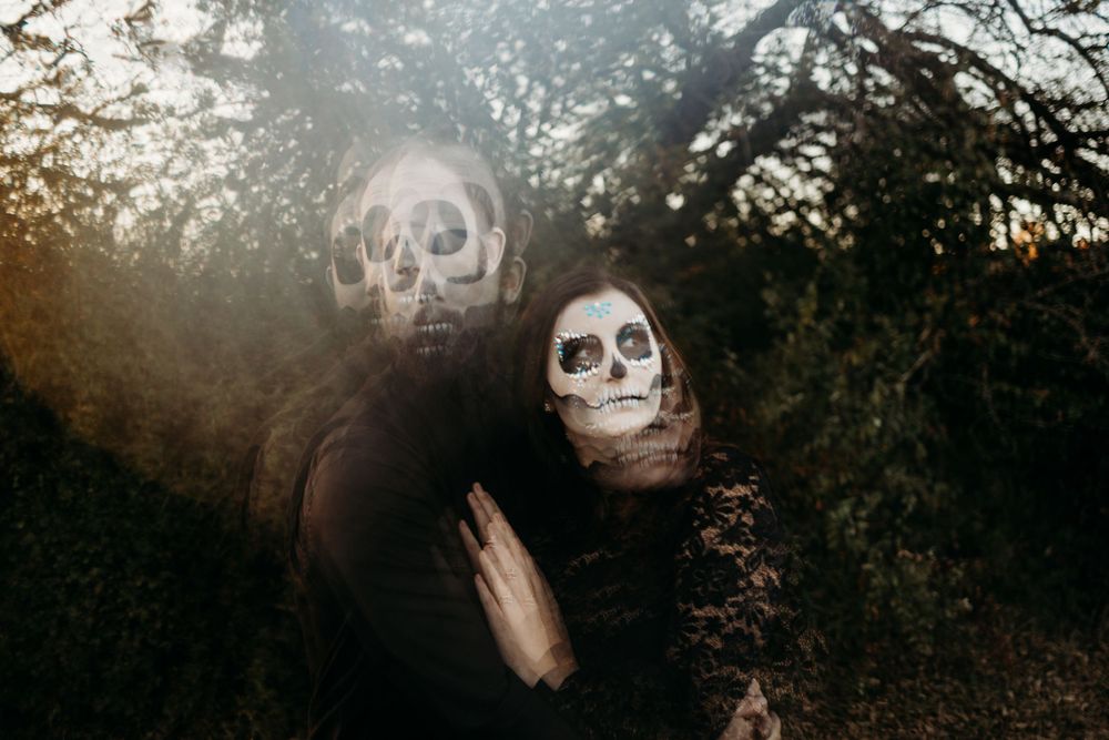 Artistic blurred double exposure of couple in skeleton makeup and black clothing among dark trees.